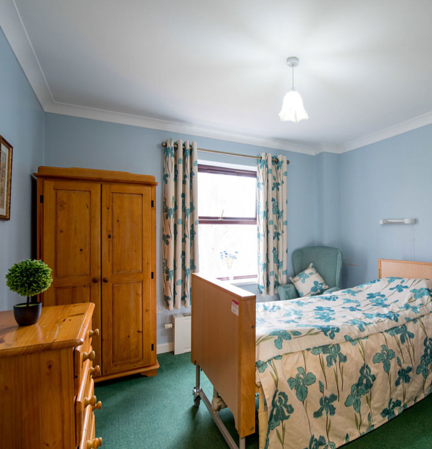 single bedroom with bed, blue armchair, chest of drawers and wardrobe