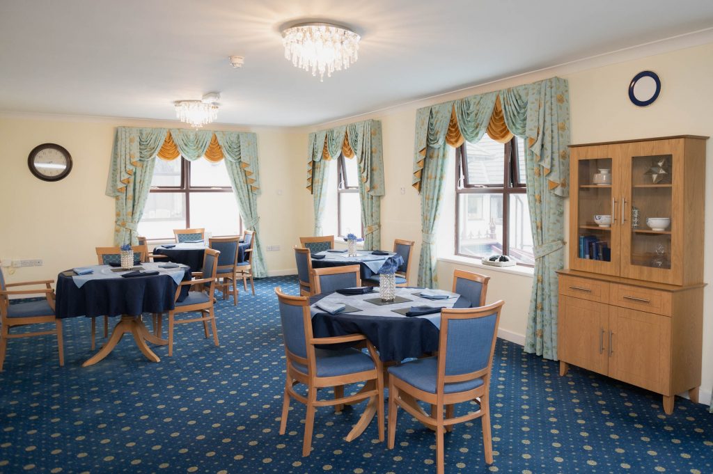 Dining area which has a blue carpet and blue and wooden dining chairs.