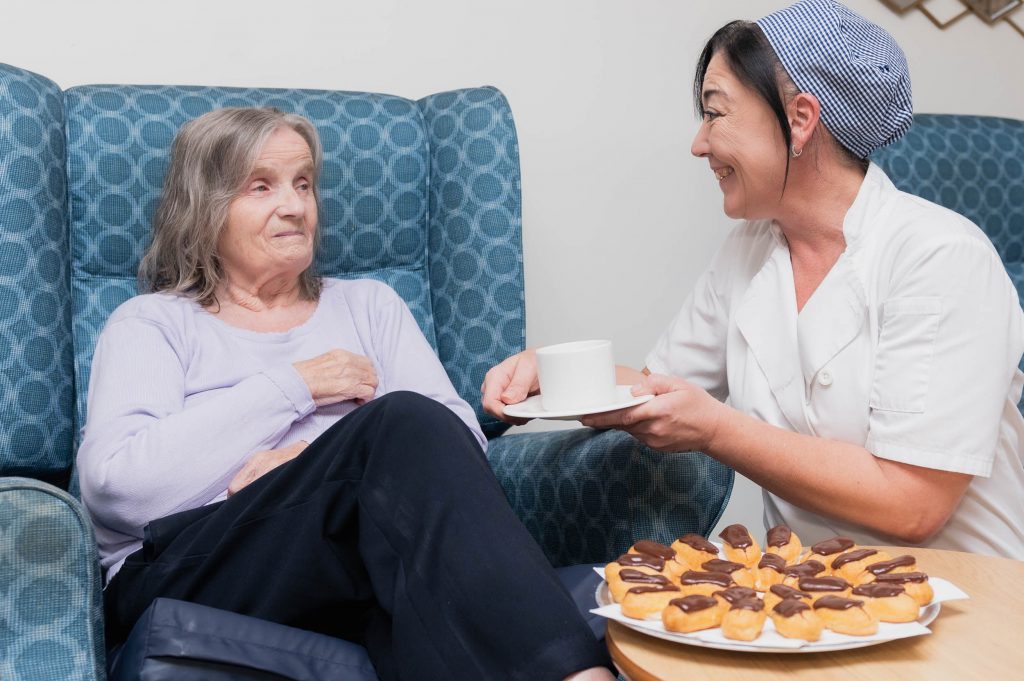 Elderly resident looking at member of staff who is holding a mug and smiling.
